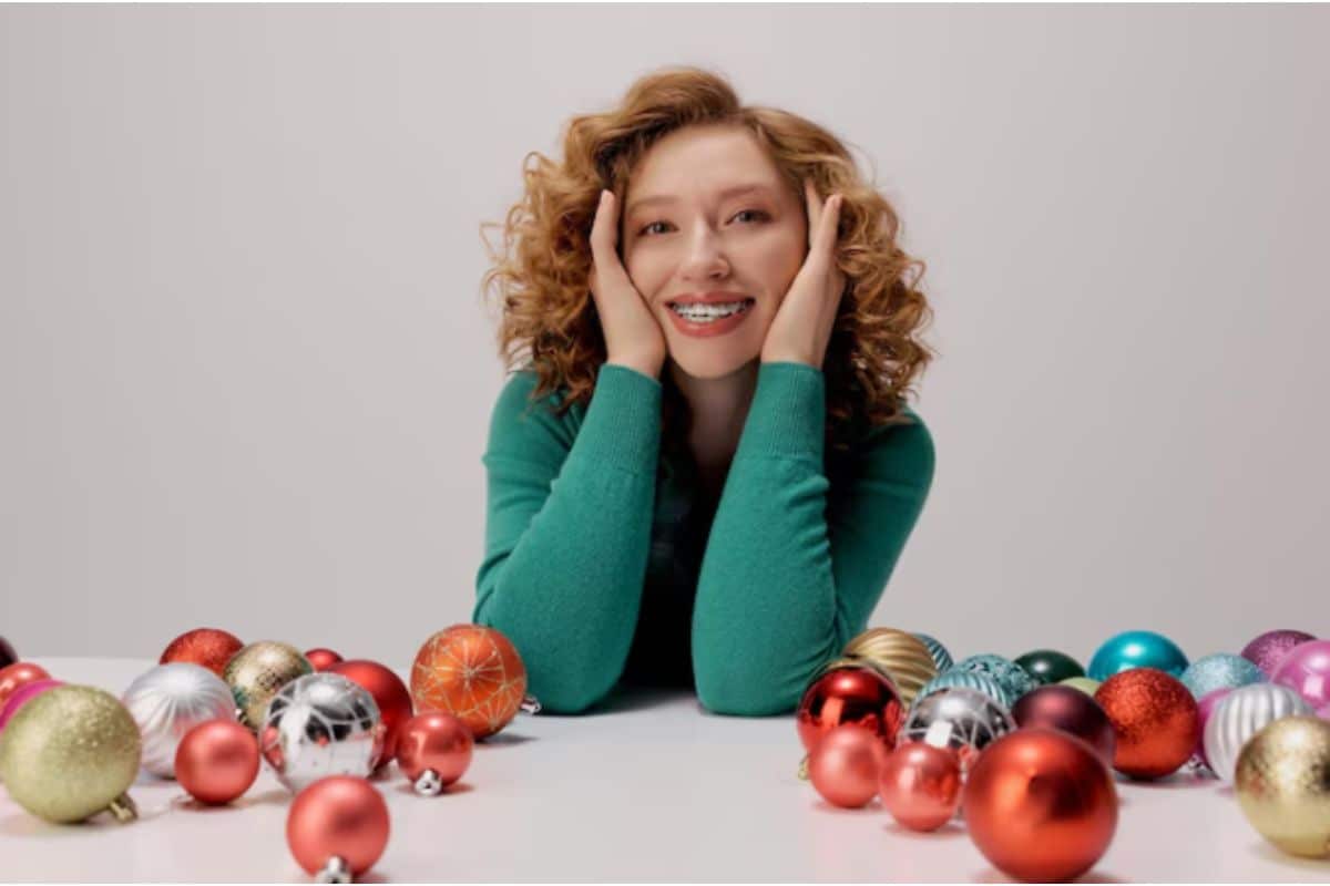 Smiling girl with braces surrounded by colorful Christmas ornaments, representing the theme of orthodontist-approved candy alternatives for the holiday season.